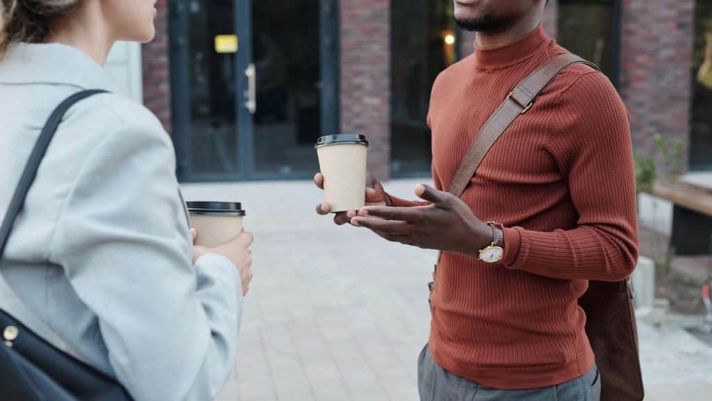 A conversation between two people holding coffee cups outdoors.