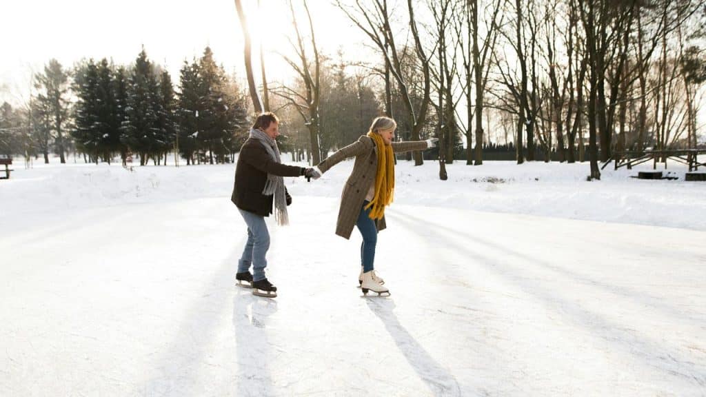 A couple ice skating together on a snowy outdoor rink.