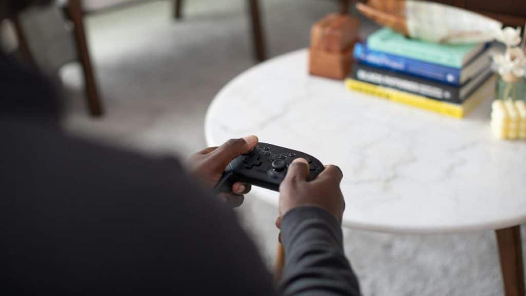 A person holding a game controller in front of a table with books.