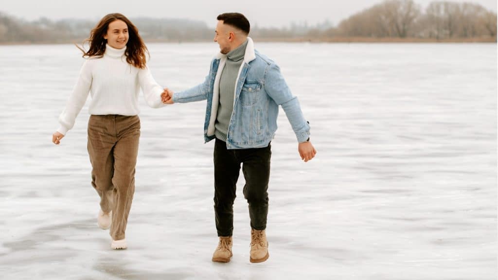 A couple walking on a snowy field and holding hands.