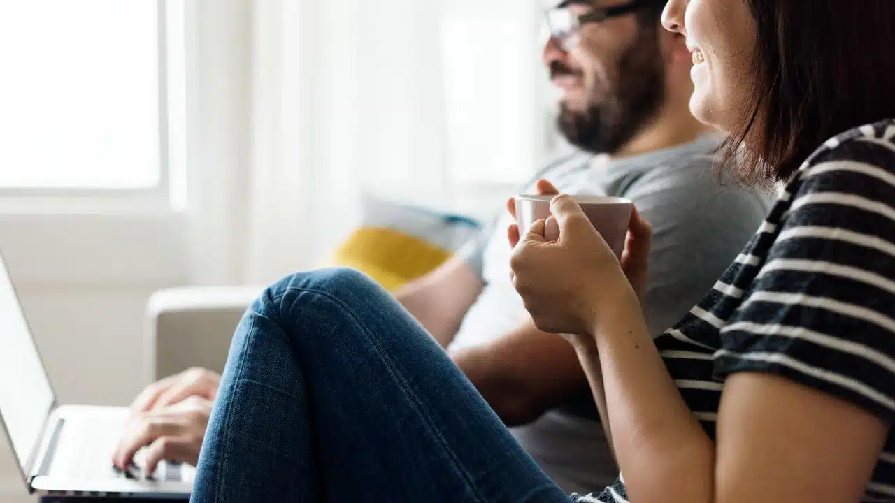 A couple relaxing on the couch with a laptop and coffee.