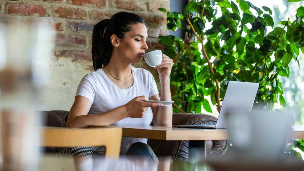 A woman drinking coffee while working on a laptop.