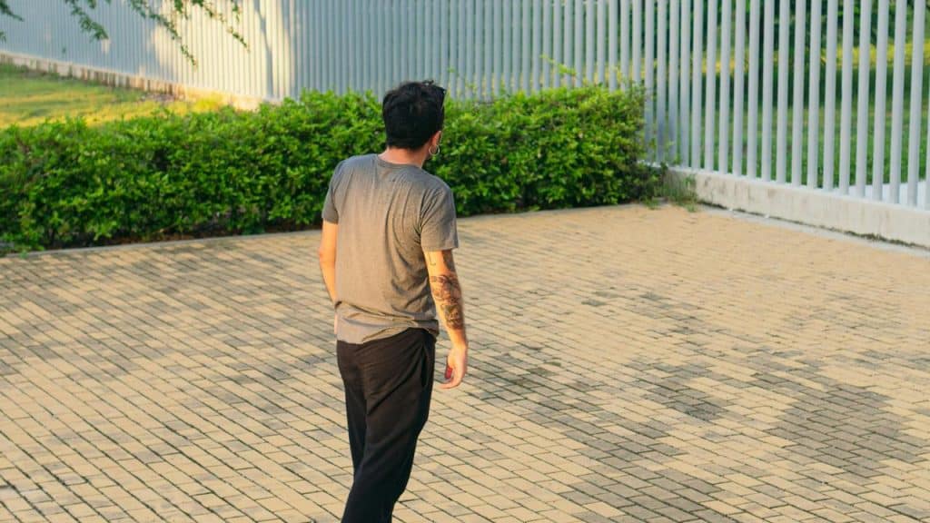 A person walking across a paved outdoor area near a fence.