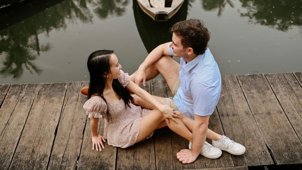 A couple sitting together on a wooden dock by the water.