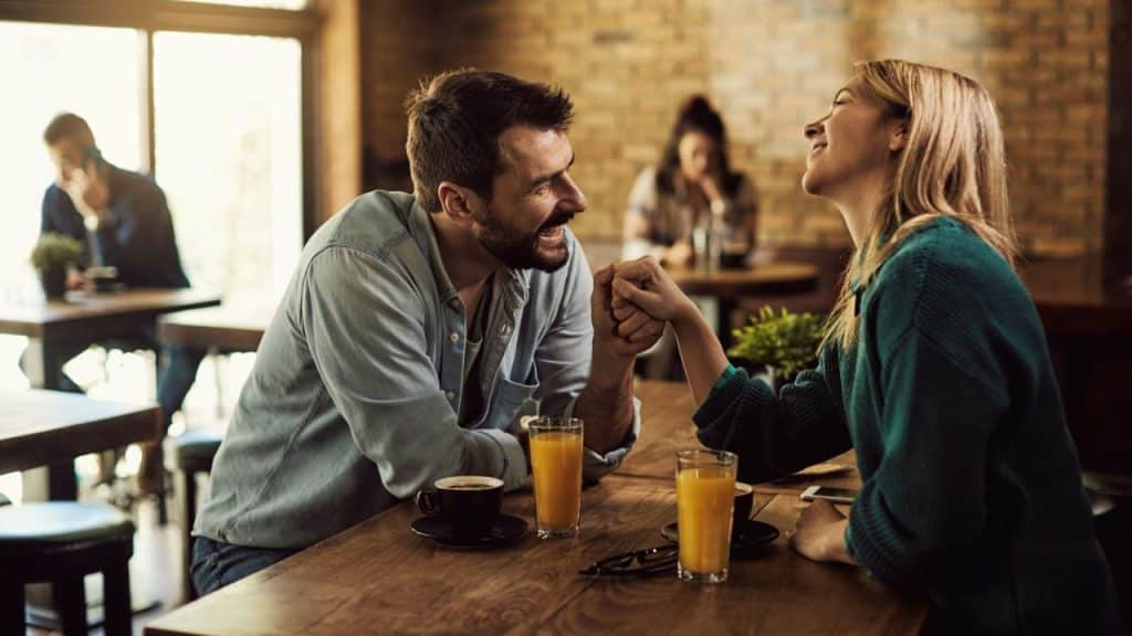 A smiling man and woman hold hands while sitting at a table with drinks.