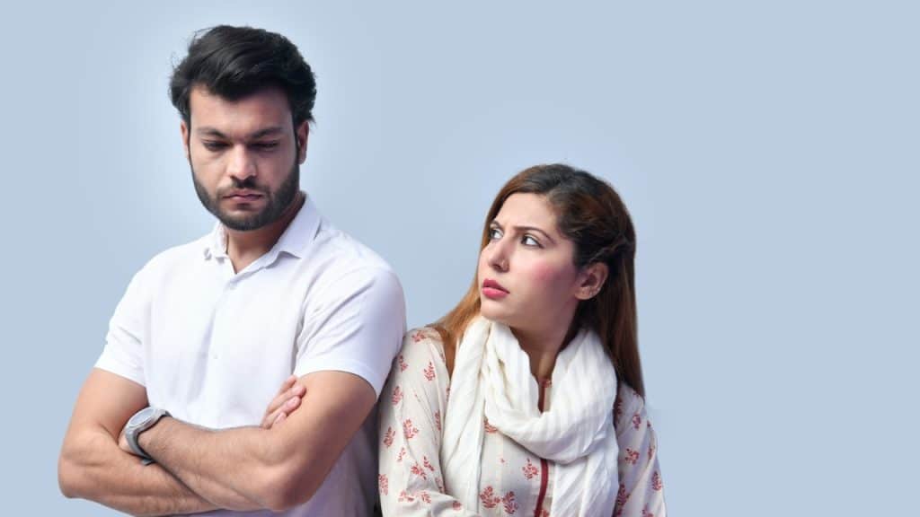 A man with crossed arms looks down while a woman beside him looks at him.