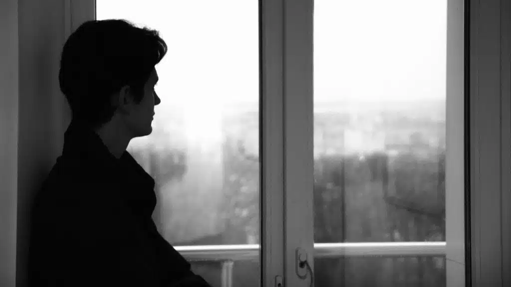 A black and white silhouette of a person looking out of a large window.