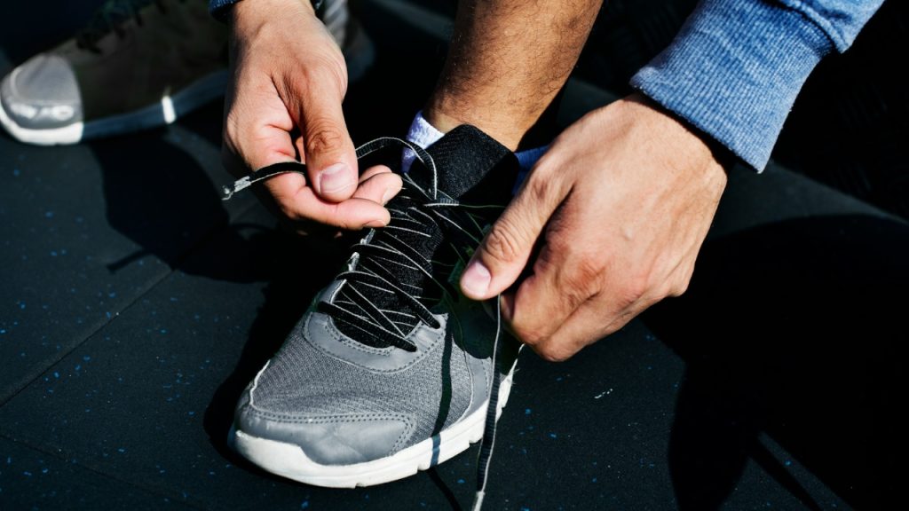 A close-up shot of a person's hands tying the laces of a gray athletic shoe.