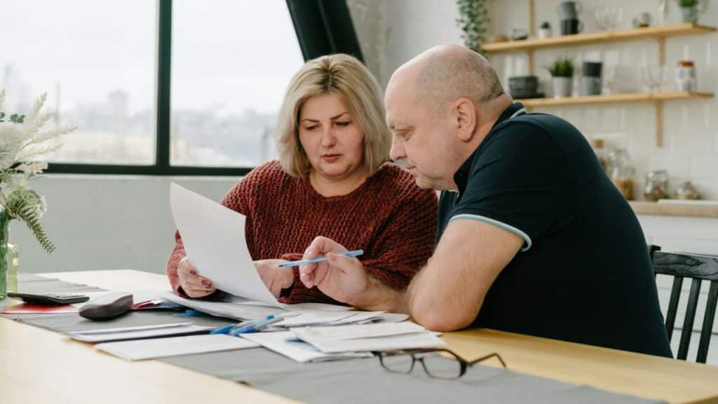 A woman and a man sit at a table looking at a paper document together.