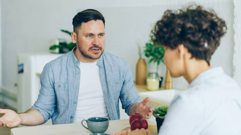 A man with an open-handed gesture speaks to a woman with short curly hair.