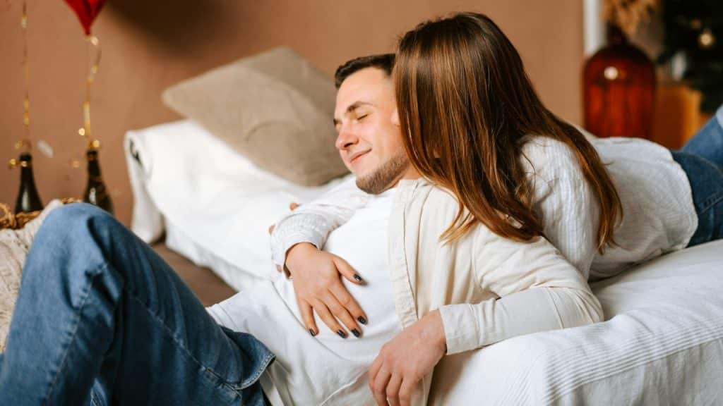 A woman lies her head on a man’s chest while they relax together on a bed.