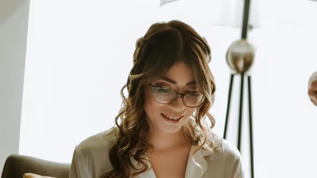 A woman with glasses smiling while looking down.