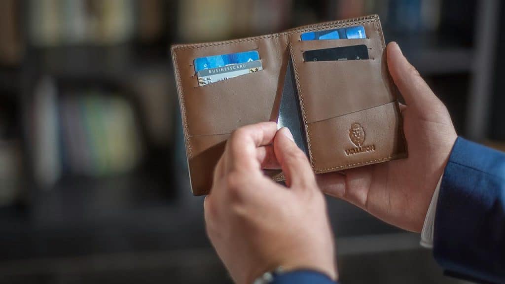 A person holding a brown leather wallet open to show several credit cards.