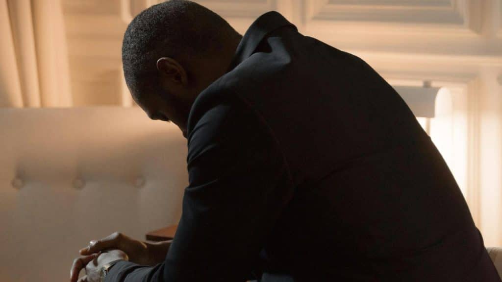 A person sits leaning forward with head bowed in a softly lit room.