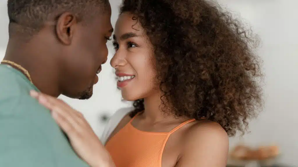 A woman with curly hair smiles while standing very close to a man.