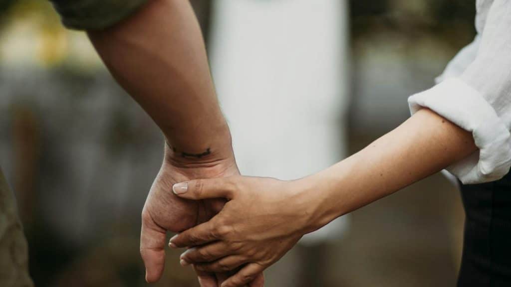 A close-up of two people holding hands outdoors.