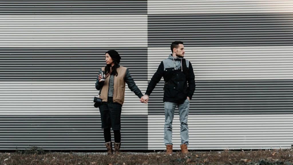 A couple holding hands while standing and looking in different directions.