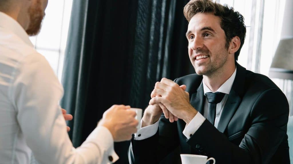 A well-dressed man smiling during a business conversation over coffee.