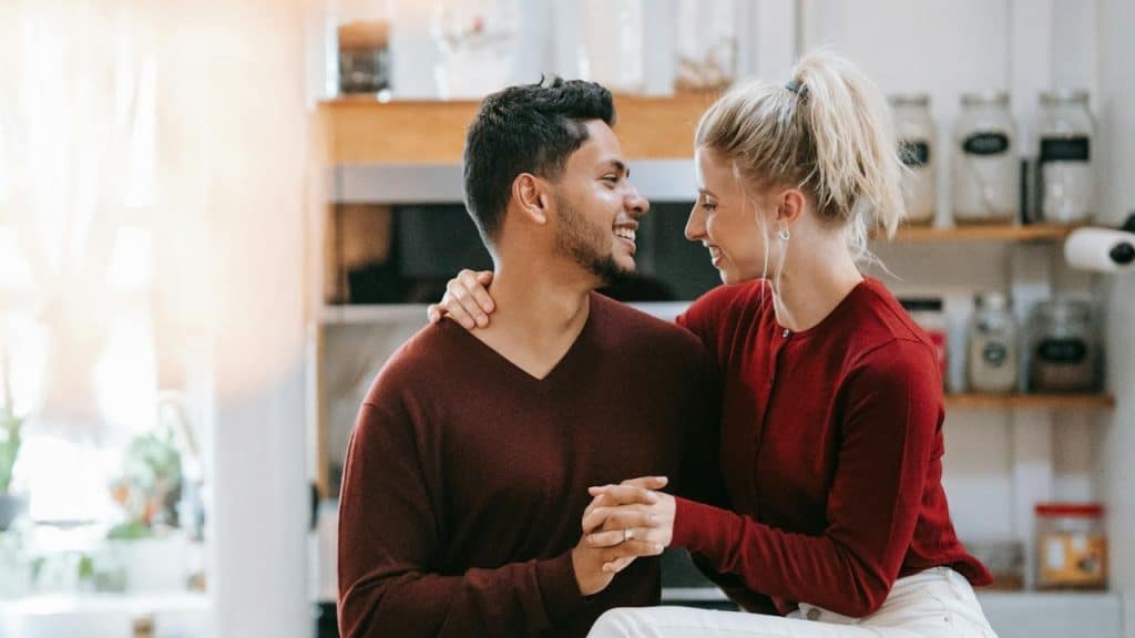 A smiling man and woman holding hands while sitting in a bright, modern kitchen setting.