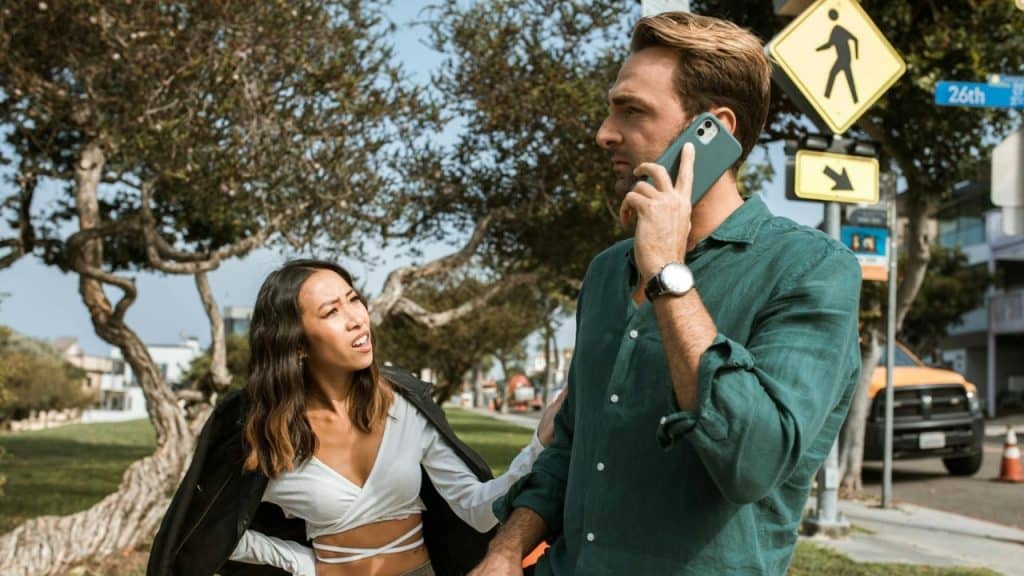 A man talks on a phone while a woman looks at him with a furrowed brow.