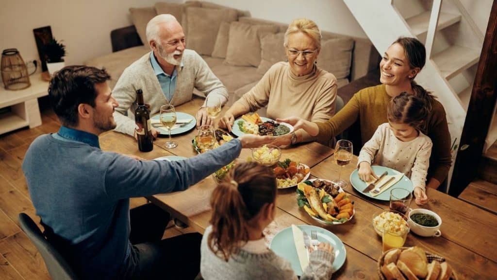 A family of six sits around a wooden table sharing a meal together indoors.