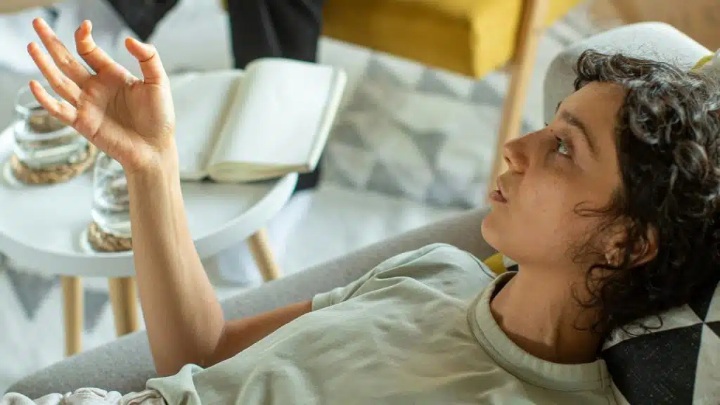 A person reclining on a couch with one hand raised, appearing thoughtful.