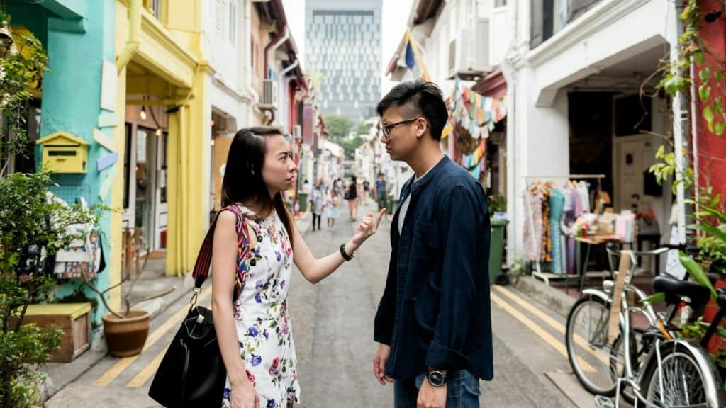 A woman in a floral dress gestures with one finger toward a man on a street.