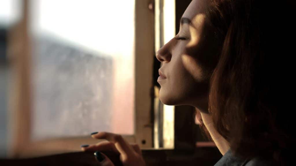 A person with eyes closed resting near a sunlit window.