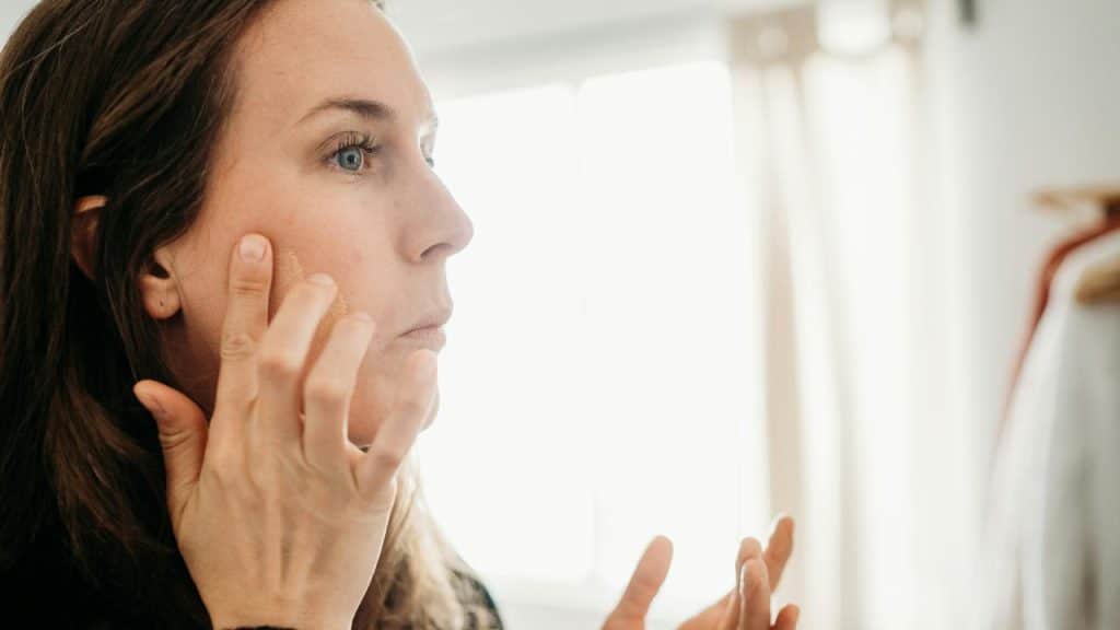 A person applying makeup to their face in soft natural light.