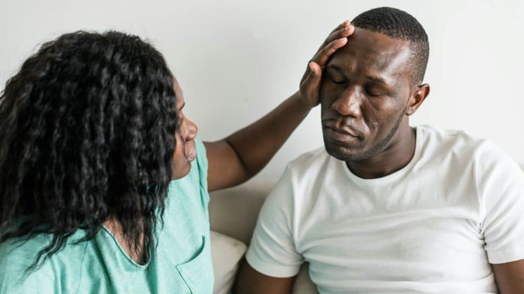 A woman in a green shirt places her hand on the forehead of a man.