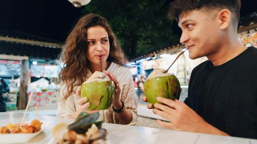 A couple sharing drinks from coconuts at a lively night market.