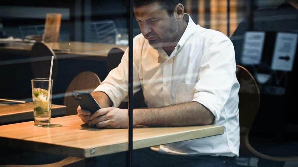 A man sitting alone at a café table looking at his phone.