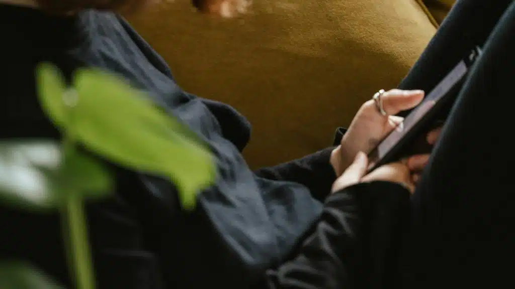 A person holding and using a tablet while sitting indoors.