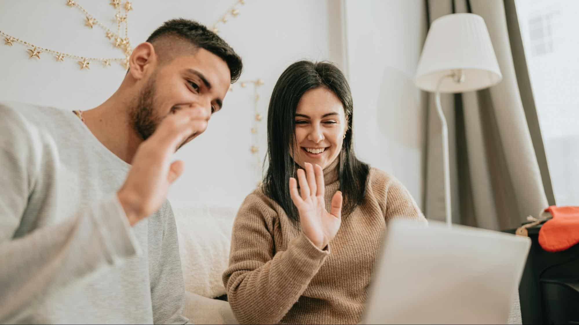 A man and woman waving at the laptop