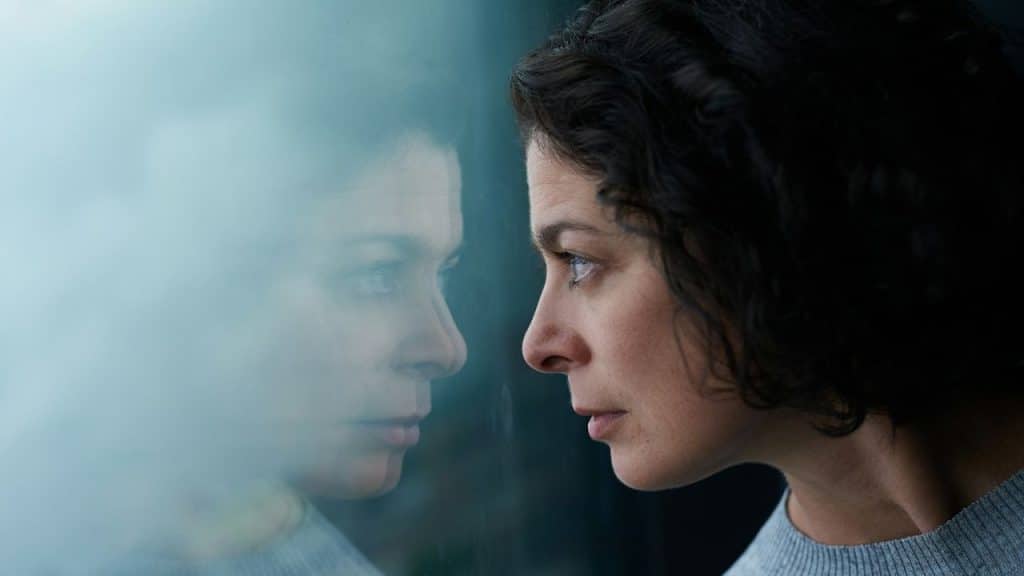 A woman with curly hair looks at her own reflection in a window pane.