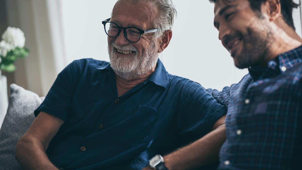 An older man smiling while sitting with a younger man.