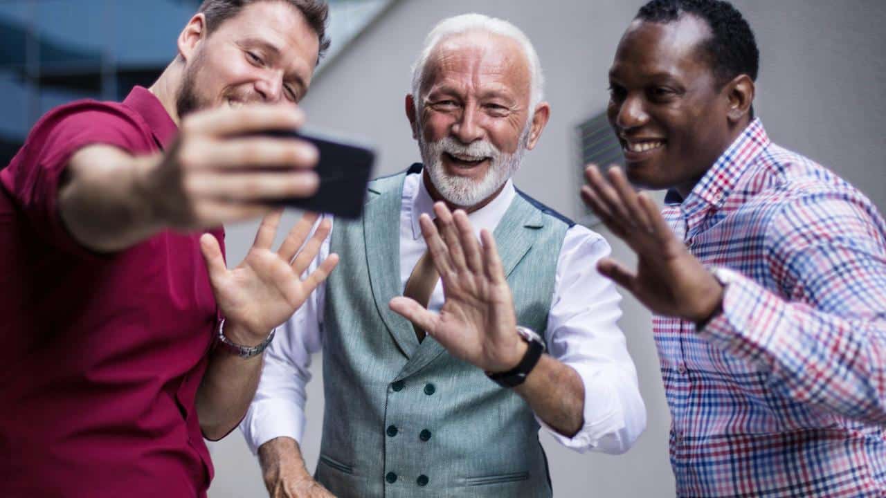 A trio of smiling men waving for a selfie.