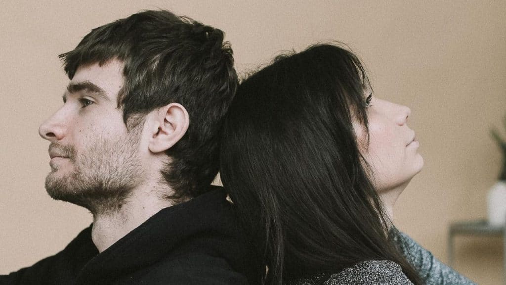 A man and woman lean their heads together back-to-back while looking in opposite directions.