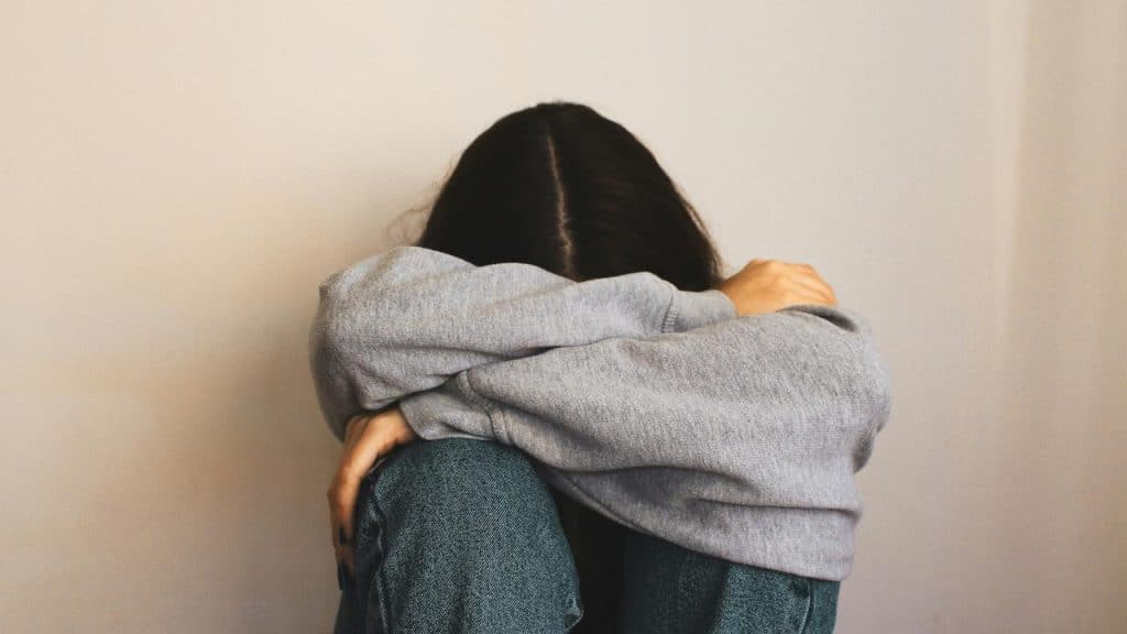A person sitting with knees pulled up and face hidden in their arms.