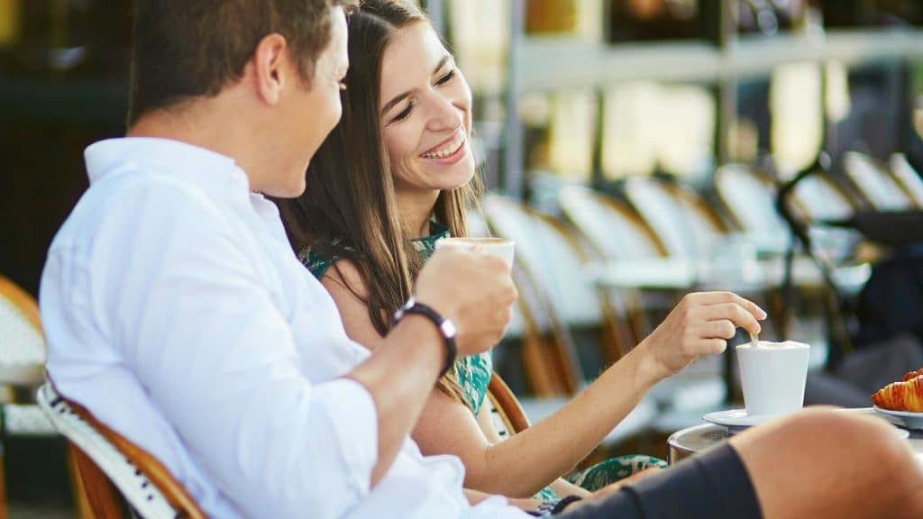 A couple smiling and enjoying coffee together at an outdoor café.