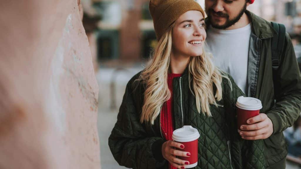 A couple walking outdoors holding takeaway coffee cups.