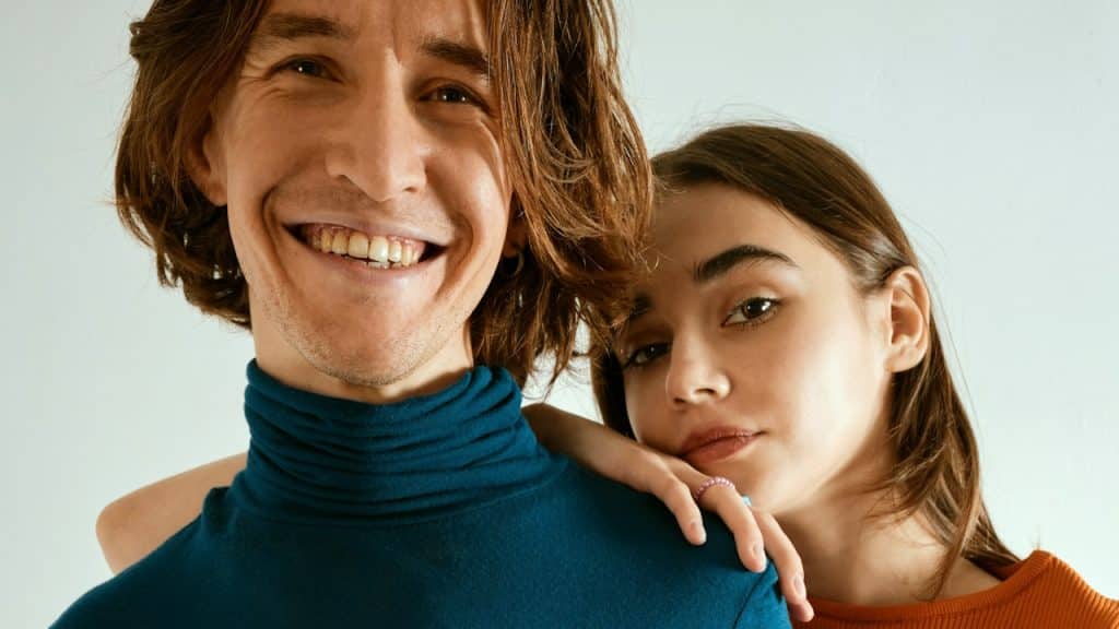 A man smiling while a woman rests her face on his shoulder with a solemn expression.