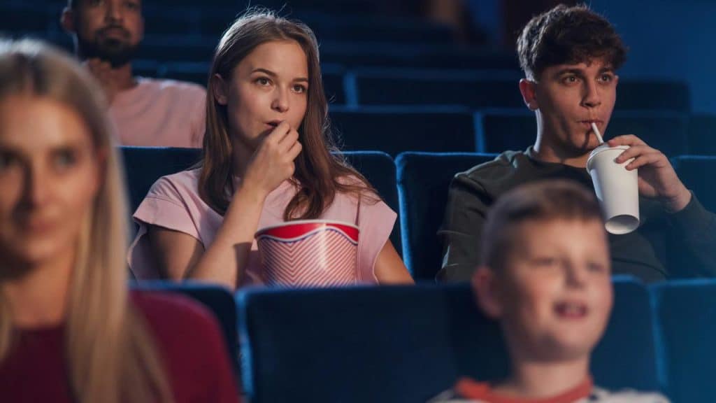 A group of people watching a movie while eating popcorn and drinking soda.