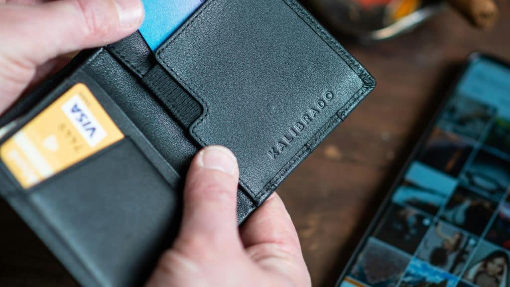 A hand holding an open black wallet with cards visible on a table.