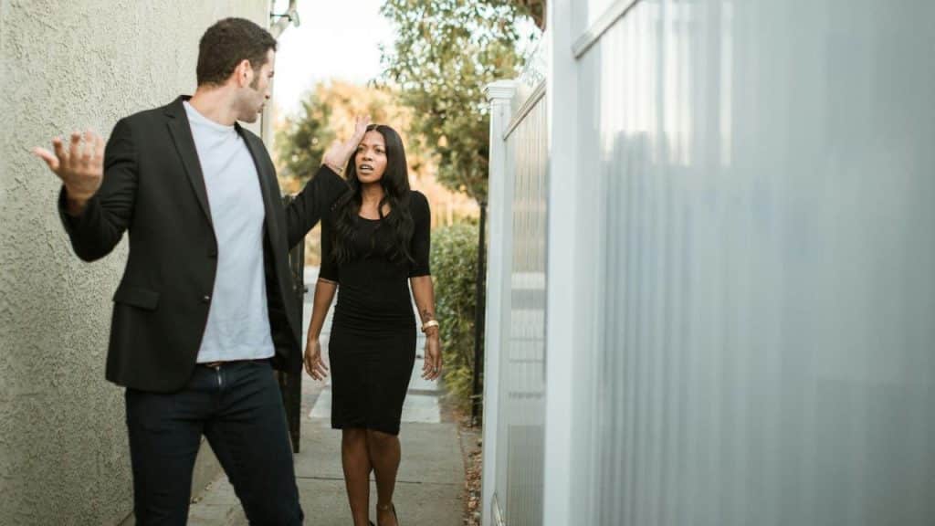 A man gestures with open arms while walking toward a woman in a black dress.