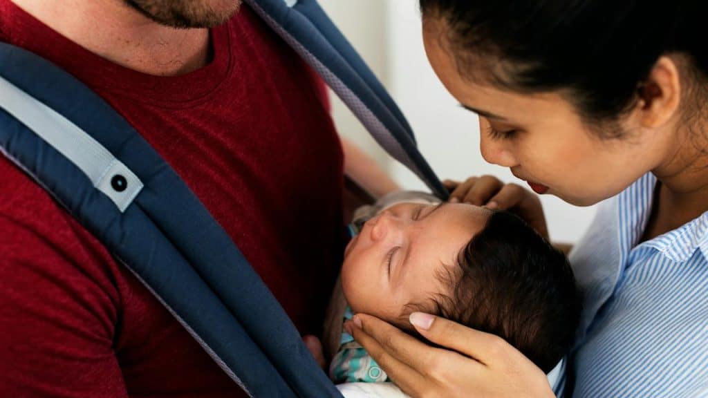 A couple gently caring for a sleeping baby in a carrier.