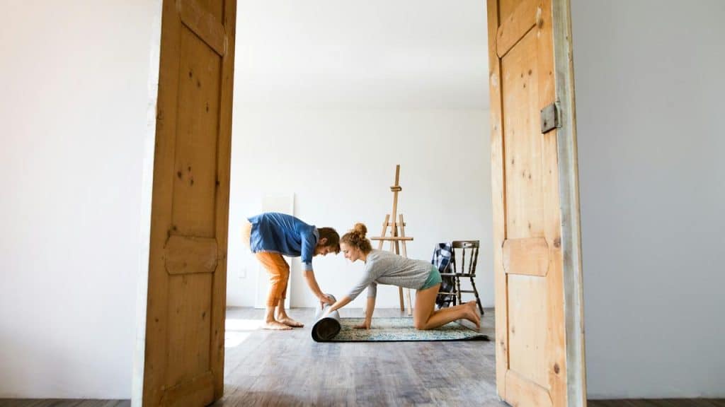 A couple unrolling a rug together in a bright, minimally furnished room.