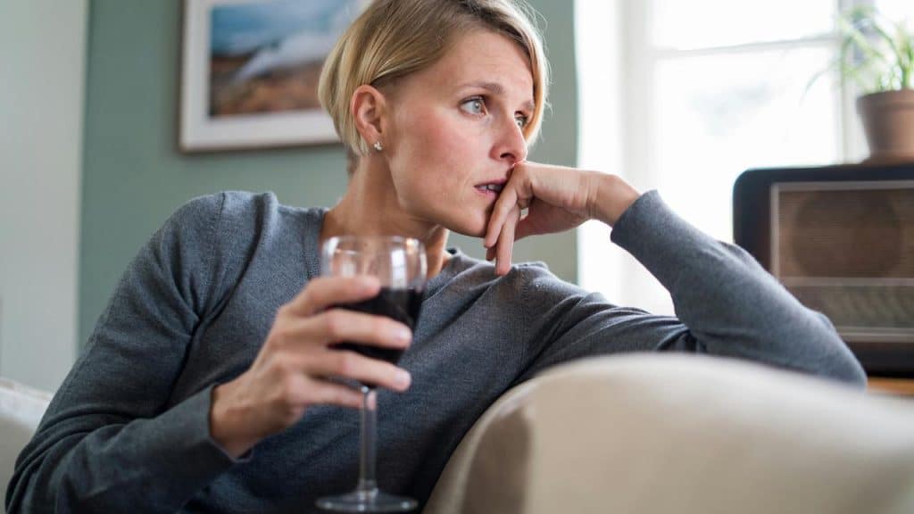 A woman holding a glass of wine while sitting and looking thoughtfully to the side.