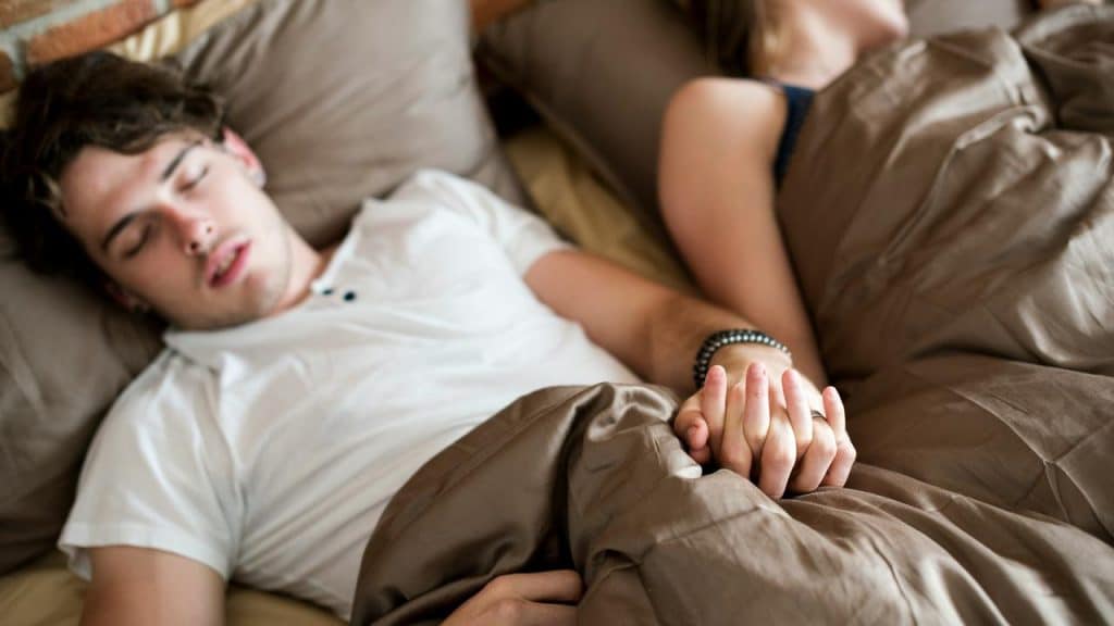 A couple sleeping in bed while holding hands.