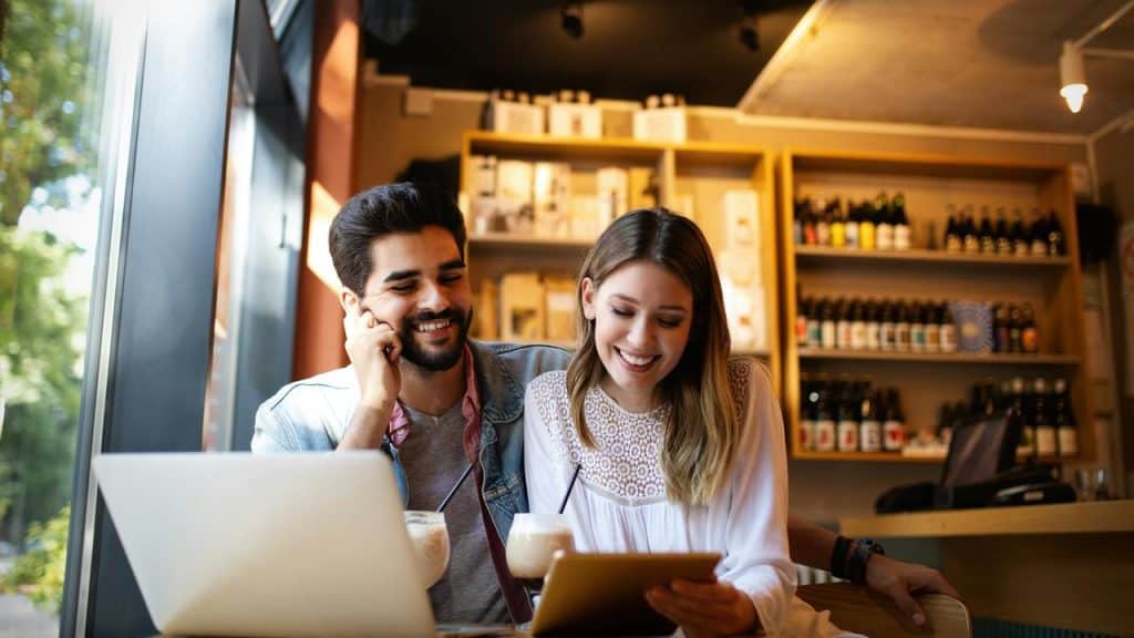 A smiling couple in a café looking at a tablet.